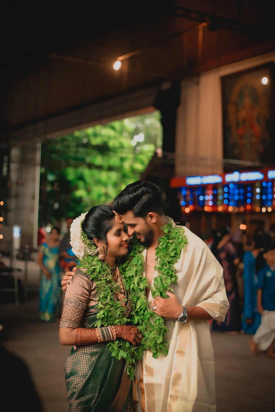 A Kerala couple in wedding dress standing close together at dusk